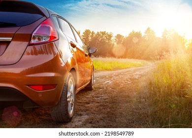 Car In The Field At Sunset. Close-up Of An Orange Car On A Country Road, Car Travel At Sunset Background, Travel From Nature By Car, Journey, Summer And Lifestyle.