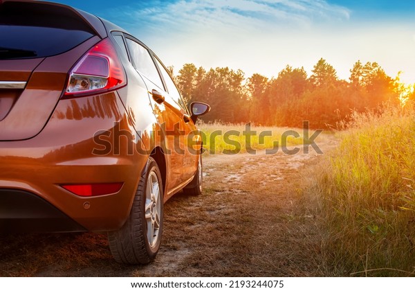 Car in the field at\
sunset. Close-up of an orange car on a country road, car travel at\
sunset background, travel from nature by car, journey, summer and\
lifestyle.