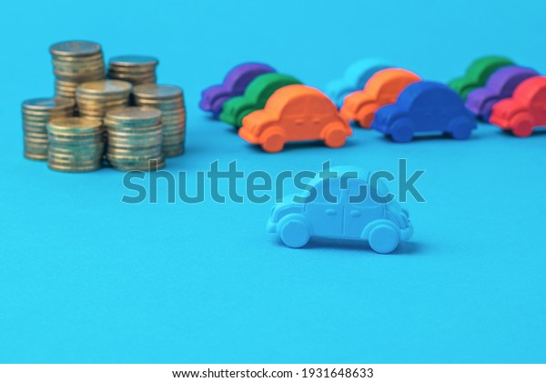 Car figurines and a stack of\
gold coins on a blue background. The concept of buying a new\
car.