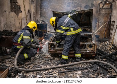 A Car Fire In Workshop Or House Garage. Firefighters Extinguishing Fire In Car With Fire Hoses And Water. Explosion And Fire Disaster. Translation : 