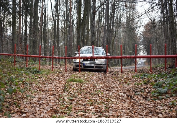 A car is in front\
of the red barrier preventing access and entrance in the forest.\
Barrier to the forest.