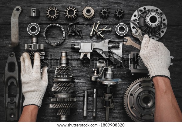 Car gearbox spare parts\
and car service worker hands with wrenches on the black flat lay\
background.