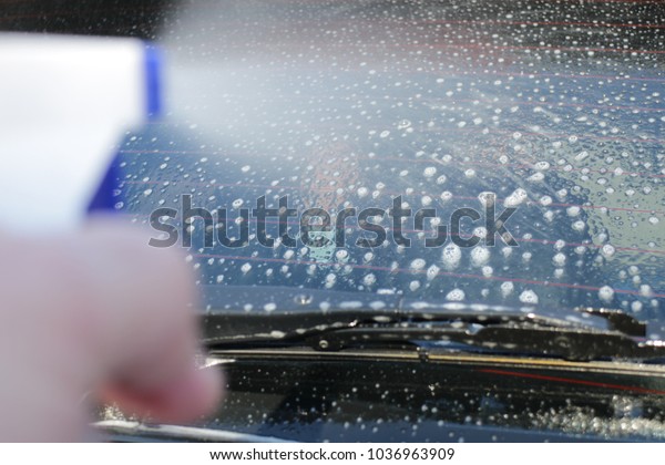 Car glass wash with spray
cleaner, rear window of the car, blur and soft focus hand with
spray