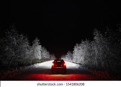 The car goes on a snowy road on a dark black night in winter. Headlights brightly illuminate the path and the forest after a snowfall - Powered by Shutterstock