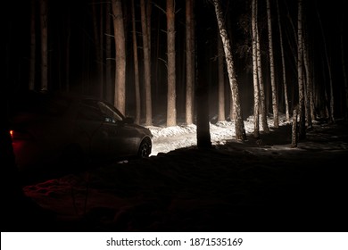 The Car Goes On A Snowy Road On A Dark Black Night In Winter. Headlights Brightly Illuminate The Path And The Forest After A Snowfall