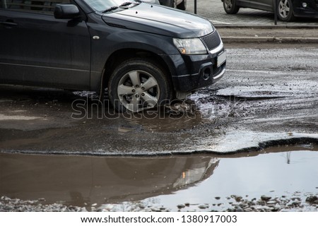 the car goes without reducing speed on a bad road with asphalt in pits and potholes, hitting the wheel in a puddle