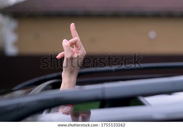The car hatch opens and a female\
driver hand with a middle finger sticks out. A woman shows an\
abusive gesture to another driver. Rudeness on the\
road.