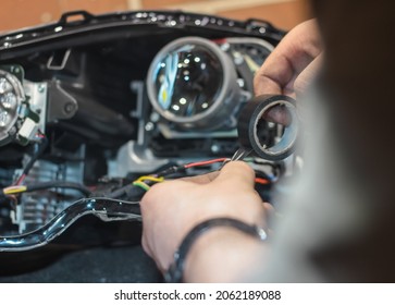 The car headlight is disassembled. Car headlight repair close-up. An auto mechanic repairs the headlight of the car. The master connects the wires in the headlight and insulates with electrical tape. 