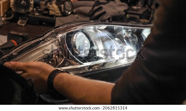 A car headlight in the hands of a man in\
close-up on a desktop background. An auto mechanic holds the\
headlight of the car. The concept of car repair in a car service.\
Dismantled headlight\
close-up.