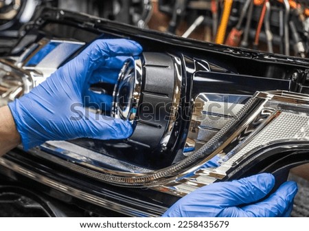 Car headlight in repair close-up. An auto mechanic wearing gloves installs the lens into the headlight housing. Installation of Bi-LED lenses in the headlight. Bi-LED lenses.