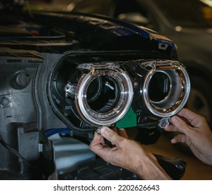 Car Headlight In Repair Close-up. The Car Mechanic Installs The Lens In The Headlight Housing. The Concept Of A Car Service.Installation Of LED Lenses In The Headlight. LED Lens.Restoration Of Optics.