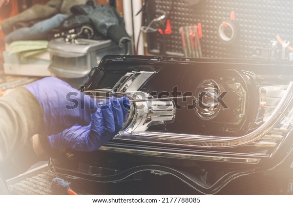 Car headlight in repair close-up. The car\
mechanic installs the lens in the headlight housing. The concept of\
a car service.Installation of LED lenses in the headlight. LED\
lens.Restoration of optics.