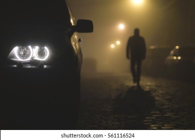 The Car Headlight With A Walking Man On The Background Of A Fog