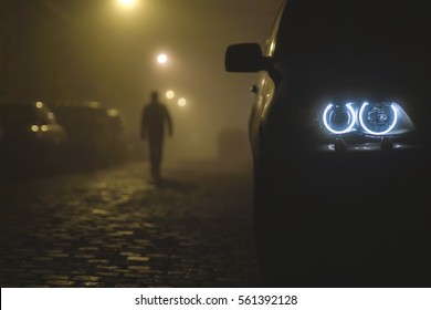 The car headlight with a walking man on a fog background. Evening-night time