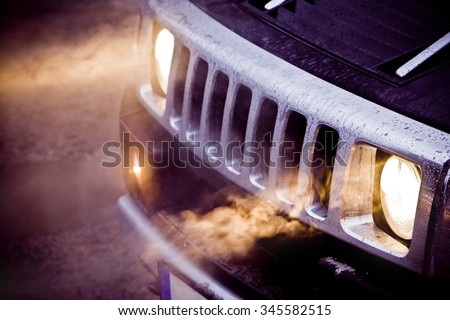 Car headlights and chrome grille of a big powerful American SUV Hummer H2. Fog in the headlights of a black expensive off road car. Bad fuel milage or economy
