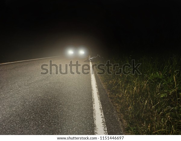 Car headlights in the dark pine wood at night.
misty road/dar highway with red lights. Driving through spooky
forest, lost highway