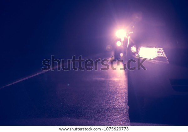 Car headlights high beam at night  with bokhe on\
the street at night time, Abstract art blurred background in dark.,\
violet tone.