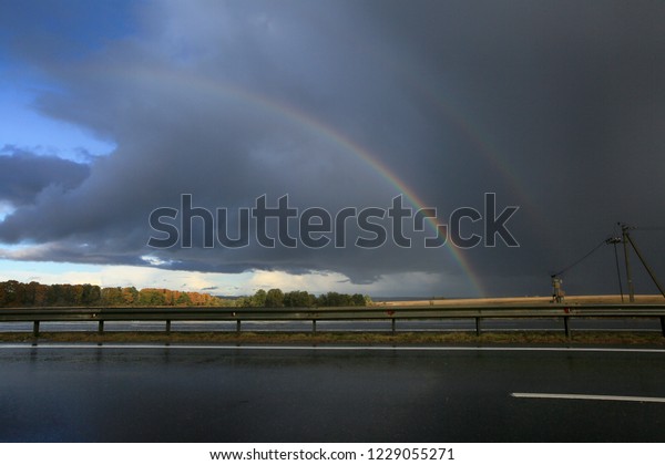 Car\
highway wet in the rain and rainbow in the\
sky