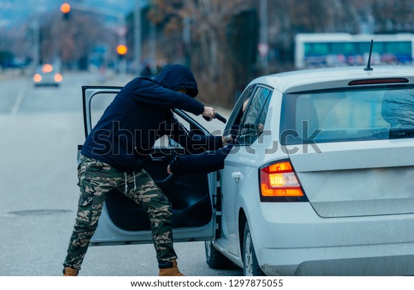 The car hijacker is pulling the car owner out of
his car and trying to get the car while pointing a loaded gun at
the drivers head.