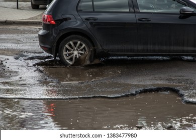 Car hitting pothole in city street splashing muddy water.