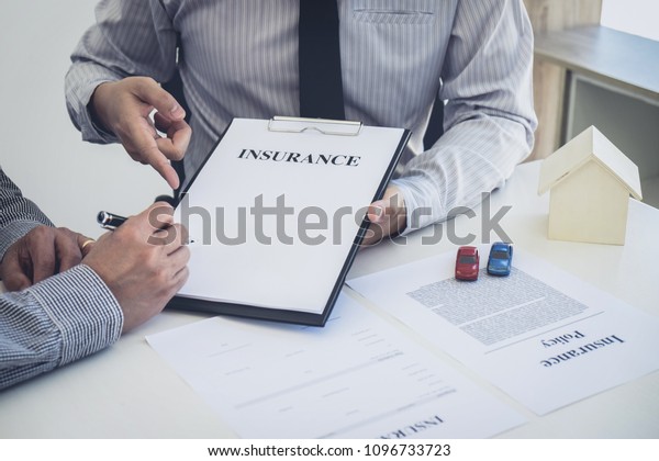 Car and Home insurance concept, broker agent\
presenting and consult to customer to decision making sign\
insurance form agreement, home and car\
model.