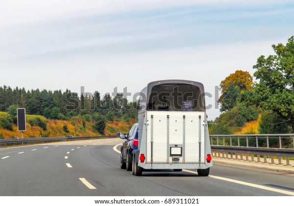 Car with\
horse trailer in the road in\
Switzerland.