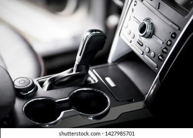 Car inside, automatic transmission close up, cup holders and armrest, black leather seats - Shutterstock ID 1427985701