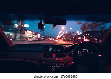 Car inside cockpit view. Neon traffic light at night on cyber punk colour concept. Driver hand hold sterring wheel drive on urban city road.