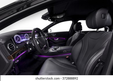 Car inside driver seat. Interior of prestige modern car. Front seat with display,steering wheel & dashboard. Black cockpit wood & metal decoration & violet ambient light on isolated white background.