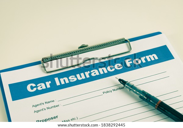 Car Insurance Claim Form or Auto Insurance Document\
and Pen at Right Frame and Clipboard on White Office Table in\
Vintage Tone