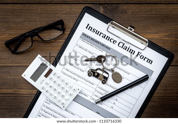Car insurance claim form\
for fill out. Empty form near car keychain on dark wooden\
background top view