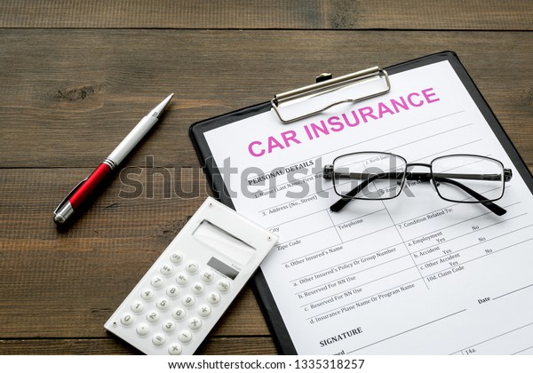 Car insurance form near glasses, calculator,\
pen on dark wooden\
background