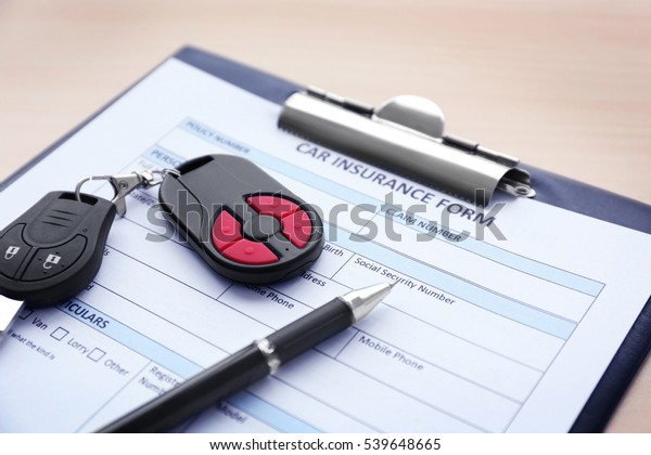 Car insurance form, pen and key on wooden table,\
close up view