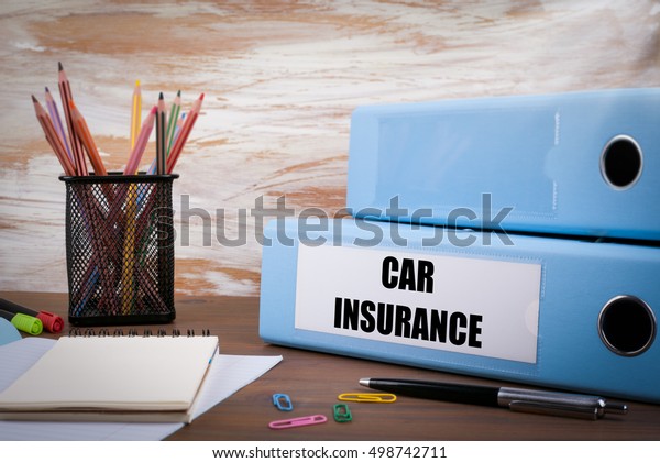 Car Insurance, Office Binder\
on Wooden Desk. On the table colored pencils, pen, notebook\
paper