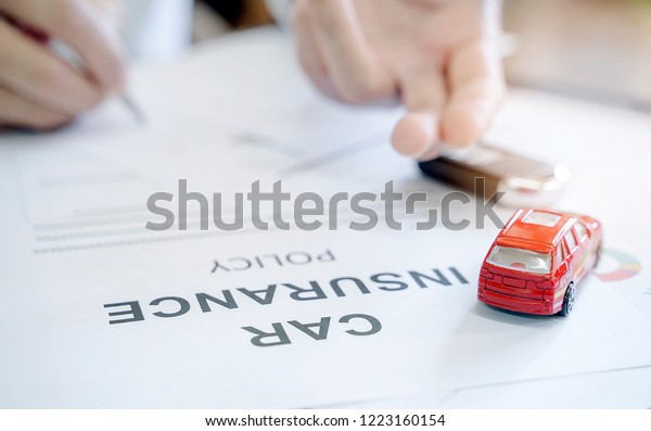 Car insurance policy\
with red car toy and blur image of man hand for vehicle insurance\
policy concept.