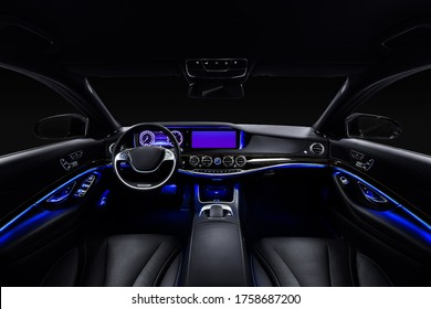 Car interior from driver seat view. Black leather cockpit with blue ambient light.