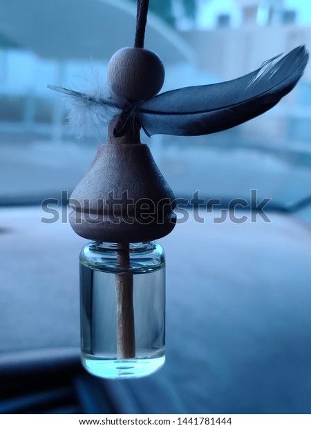 Car interior fragrance freshener bottle \
 and\
feather hanging on the rear view mirror. Small glass bottle with\
wooden lid and aromatic\
perfume.