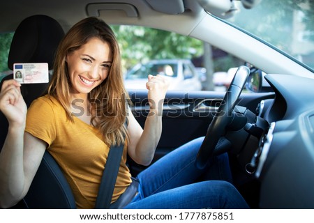 Car interior view of woman with driving license. Driving school. Young beautiful woman successfully passed driving school test. Female smiling and holding driver's license.