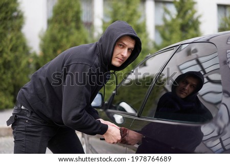 Car jacking thief steal car breaking door criminal job burglar Hijacks  Auto thief black balaclava hoodie trying  break into vehicle screwdriver  Street crime violence gangster