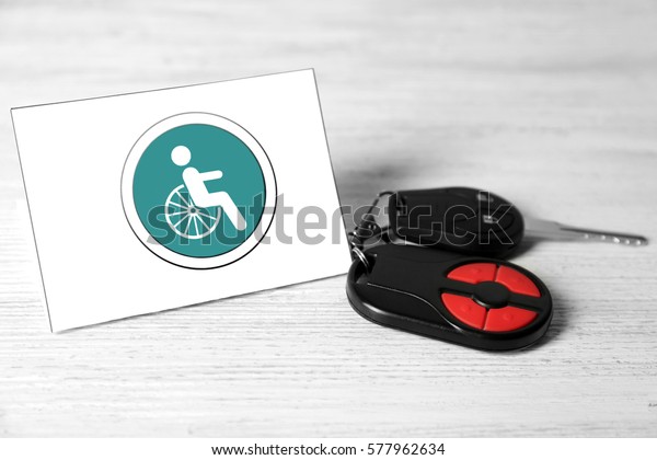 Car key and card with handicap sign on light\
wooden background