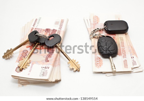 Car key and home keys over stacks of paper\
money on white background