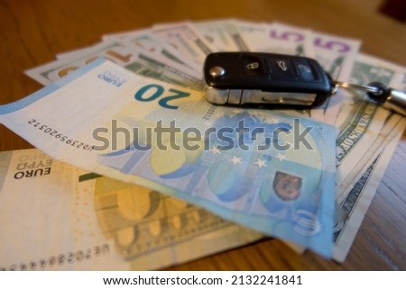 Car key lying on a bundle of dollar bills. Increase in fuel prices resulting in higher expenses related to the use of the car.