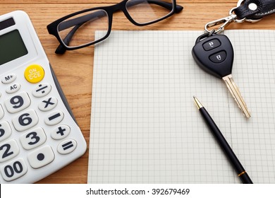 Car key on blank notebook with calculator and pen on wood table