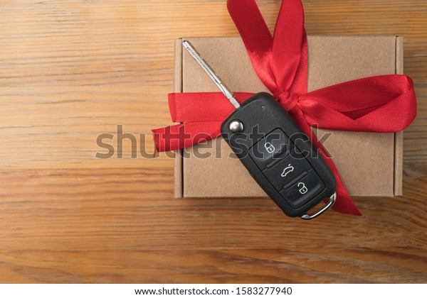 Car key on a paper box with red bow on natural\
wooden table background. Christmas or Valentine\'s Day gift or\
present abstract concept.