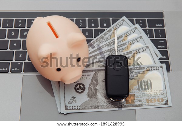 Car\
key and piggy bank with money on a laptop\
keyboard