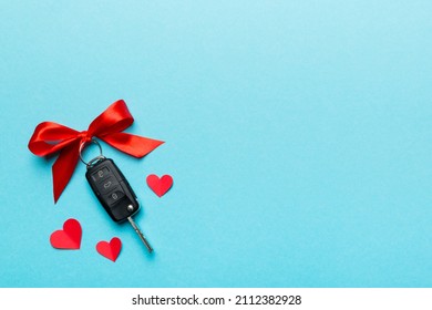 Car key with a red bow and a heart on Colored table. Giving present or gift for valentine day or christmas, Top view with copy space.