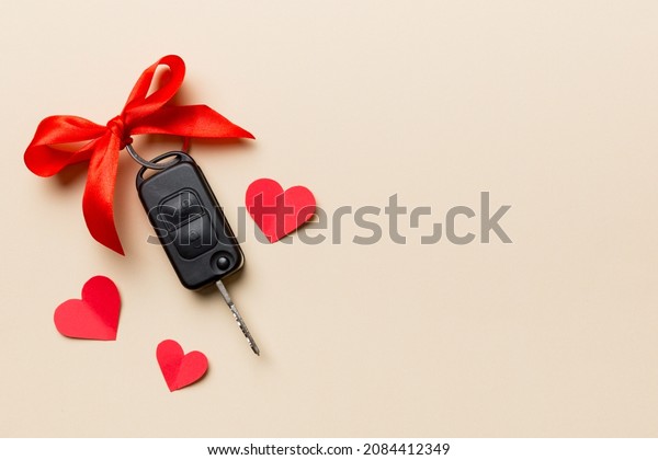 Car key with a red bow and a heart on Colored\
table. Giving present or gift for valentine day or christmas, Top\
view with copy space.