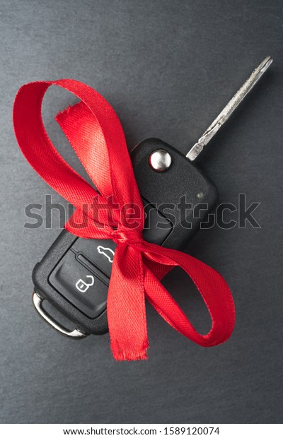 Car key with red bow on\
dark black slate plate background. Christmas or Valentine\'s Day\
gift or present abstract concept. Vertical orientation. Flat lay\
top view.