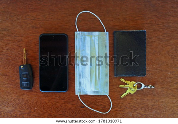 Car\
key, Smartphone, Surgical mask, Wallet and Keys top view\
composition with wooden table background. JUL\
2020