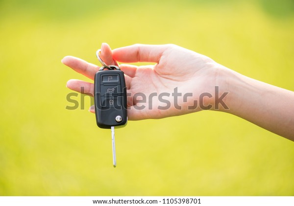 car key in\
woman hand and green grass\
background